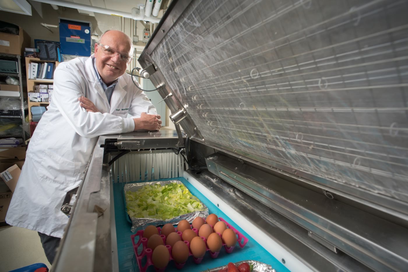 Dr. Keith Warriner beside the open treatment chamber in his University of Guelph laboratory, with lettuce and eggs on the belt