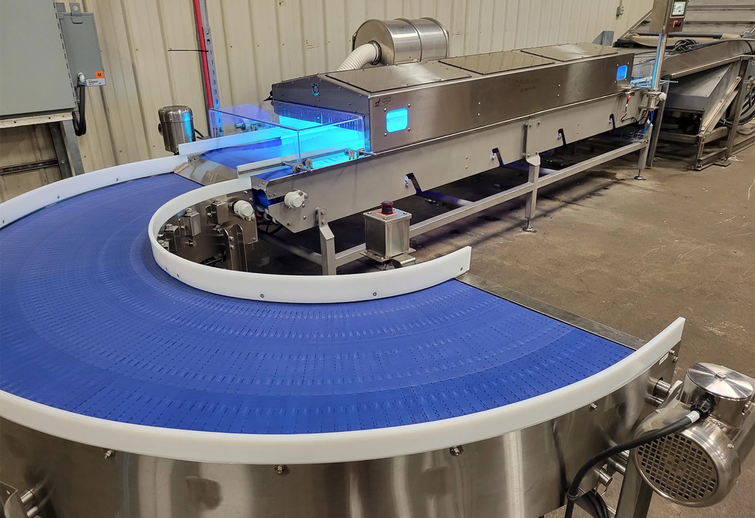 Clean Flow treatment tunnel glowing with UV-C light above a curved blue conveyor in a packing facility