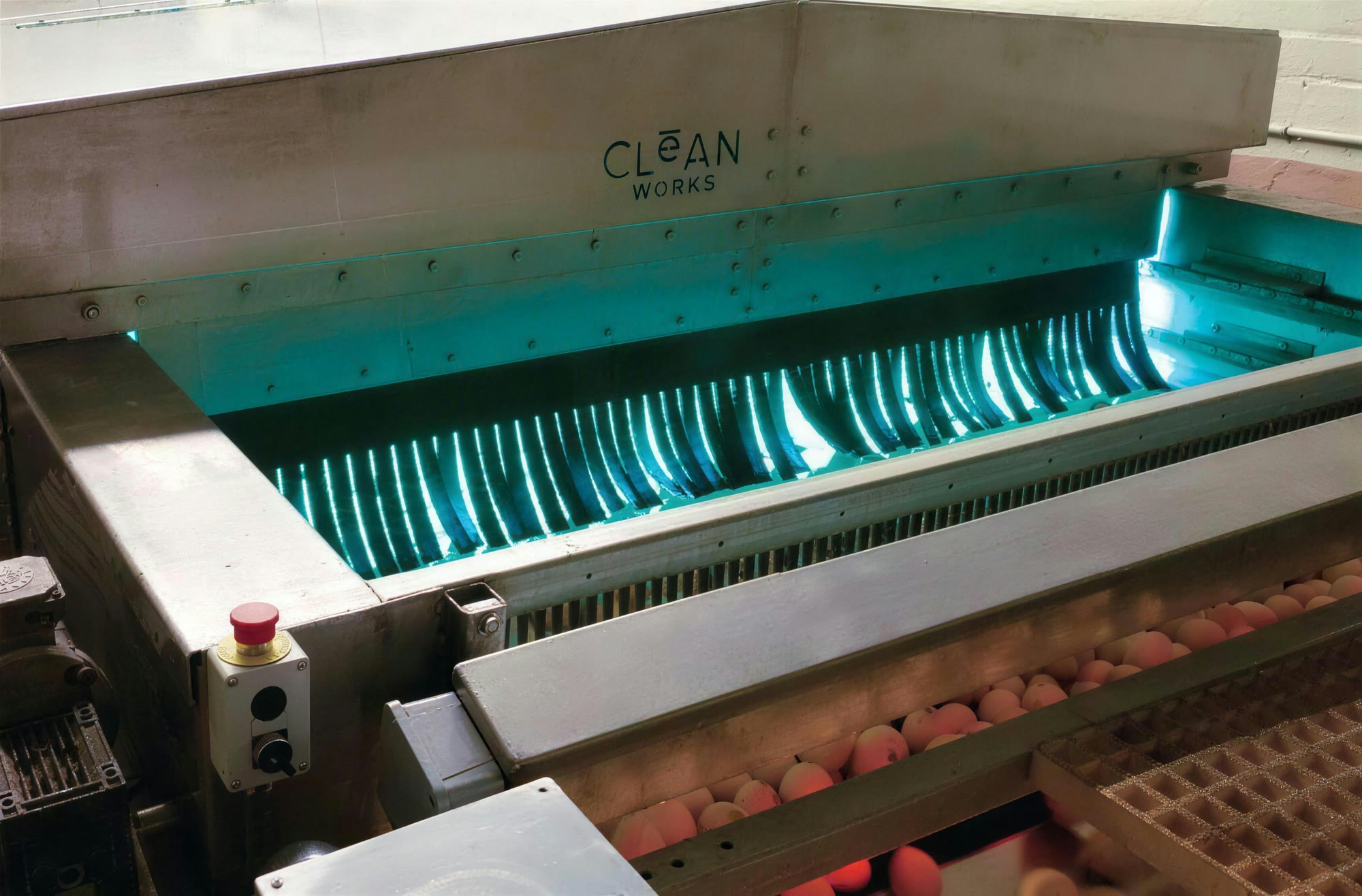 UV-C light glowing inside an open Clean Works treatment chamber above a produce conveyor
